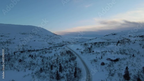 Mountain area with cottages covered in snow, mountain road and frozen mountain lake in a far.  Drone footage, sunset time photo