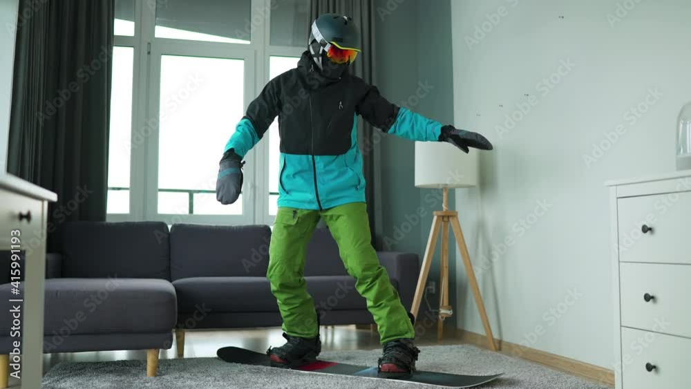 Fun video. Man dressed as a snowboarder depicts snowboarding on a carpet in a cozy room. Waiting for a snowy winter Fun video. Man dressed as a snowboarder depicts snowboarding on a carpet in a cozy room. Waiting for a snowy winter