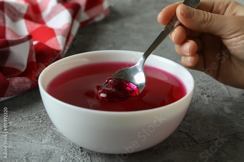Female hand hold spoon in bowl of red jelly on gray table