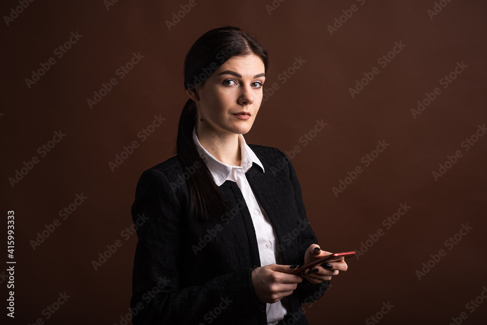 Portrait of a business woman who uses her smartphone in the studio on a brown background Portrait of a business woman who uses her smartphone in the studio on a brown background