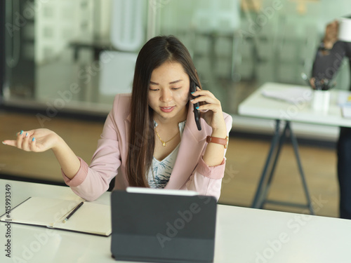 Businesswoman talking on the phone while working with digital tablet in office room