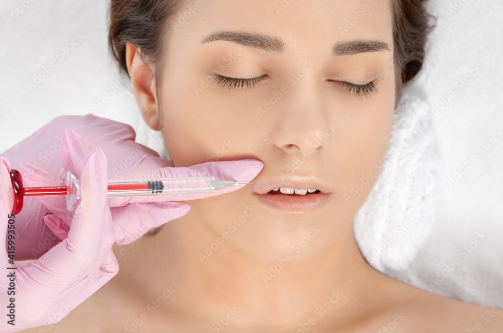 Cosmetologist does injections for lips augmentation and anti wrinkle in the nasolabial folds of a beautiful woman. Women's cosmetology in the beauty salon. Cosmetologist does injections for lips augmentation and anti wrinkle in the nasolabial folds of a beautiful woman. Women's cosmetology in the beauty salon.