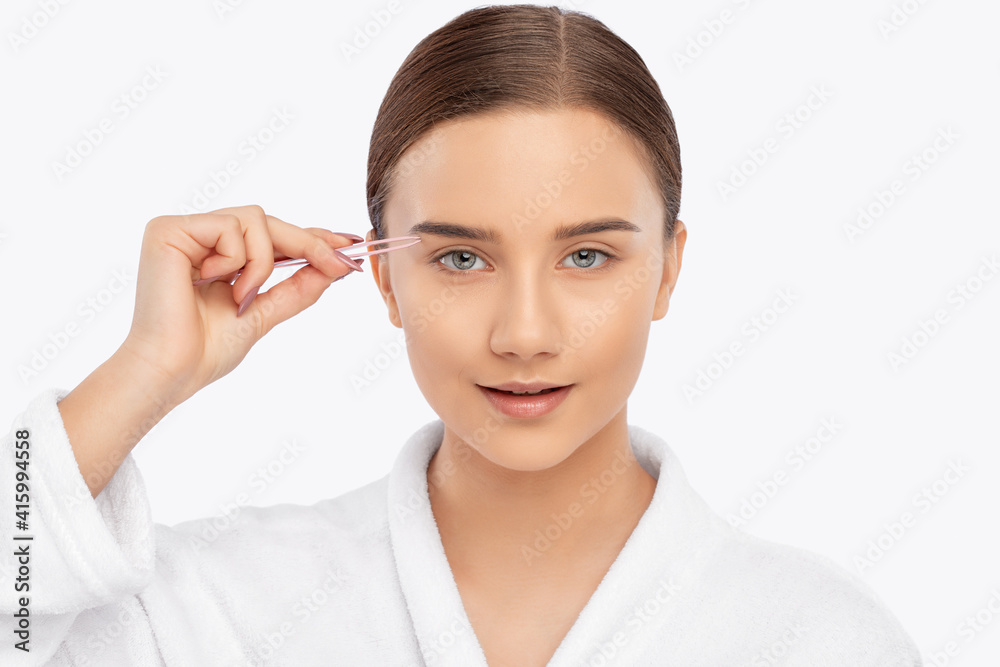 Young attractive woman in a white coat plucking eyebrows. Professional make-up and cosmetic skin care. Young attractive woman in a white coat plucking eyebrows. Professional make-up and cosmetic skin care.