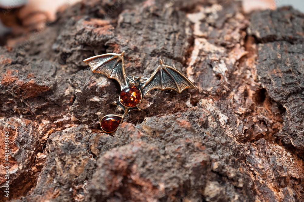 A brooch in the form of a bat made of bronze and amber against the background of birch slice A brooch in the form of a bat made of bronze and amber against the background of birch slice