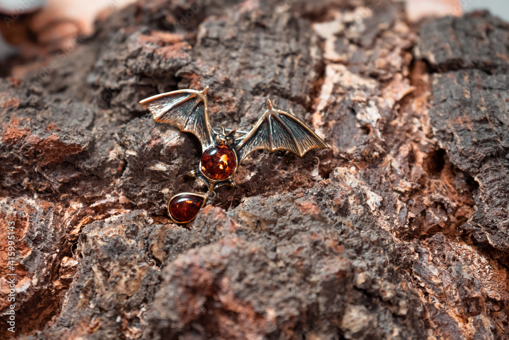 A brooch in the form of a bat made of bronze and amber against the background of birch slice