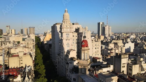 Aerial dolly out of Barolo Palace tower and Buenos Aires buildings on tree-lined Avenida de Mayo at sunset photo