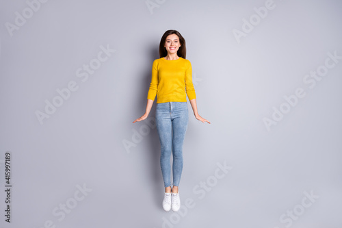 Full size photo of optimistic brunette nice lady jump wear yellow sweater jeans sneakers isolated on grey color background