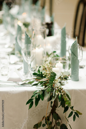 Elegant table setting in restaurant. Wedding banquet  in green and pale blue with floral decoration on table, natural green branch, white candles, silver cutlery. Closeup view