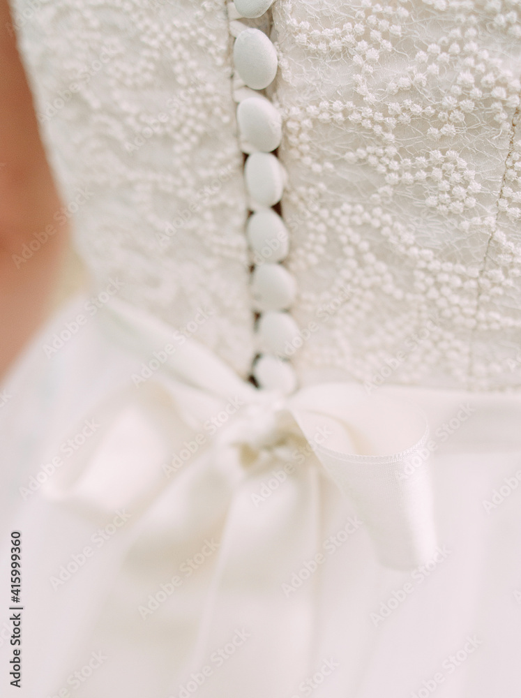 White wedding dress close up. Elegant lace, bow and small fabric-covered buttons, bridal details macro.