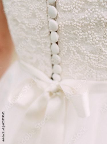 White wedding dress close up. Elegant lace, bow and small fabric-covered buttons, bridal details macro.