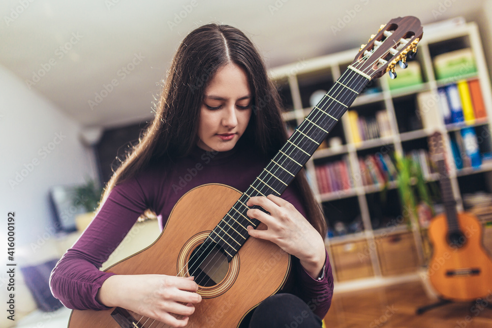 Fototapeta premium Pretty girl practicing some new sound on a guitar at home