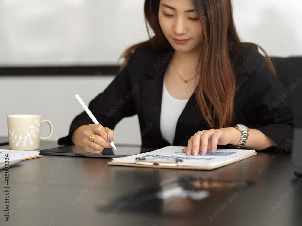 Businesswoman analysing business document and noting on digital tablet in office room Businesswoman analysing business document and noting on digital tablet in office room