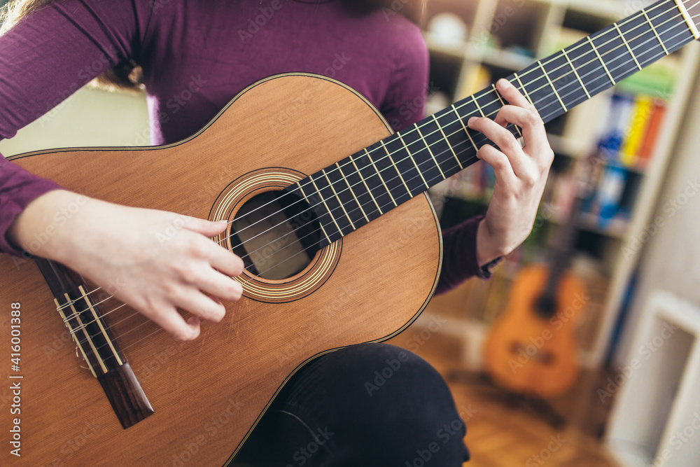 Fototapeta premium Girl practicing some new sound on a guitar at home, close up.