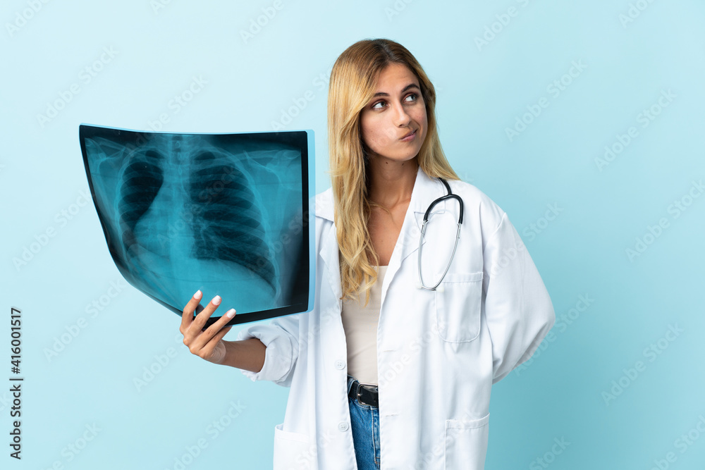 Young blonde Uruguayan doctor woman isolated on blue background and looking up Young blonde Uruguayan doctor woman isolated on blue background and looking up