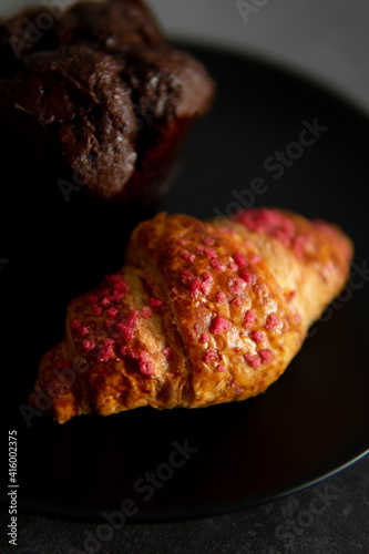 croissant with raspberries and chocolate muffin on a black plate.