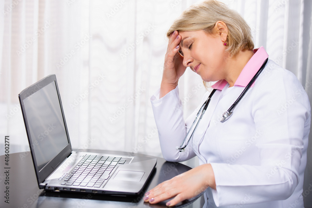 Doctor in a white coat with a stethoscope,thinking. Senior female doctor is tired. The medical worker was overworked from full graphic of online consultations on white medical office background. Doctor in a white coat with a stethoscope,thinking. Senior female doctor is tired. The medical worker was overworked from full graphic of online consultations on white medical office background.