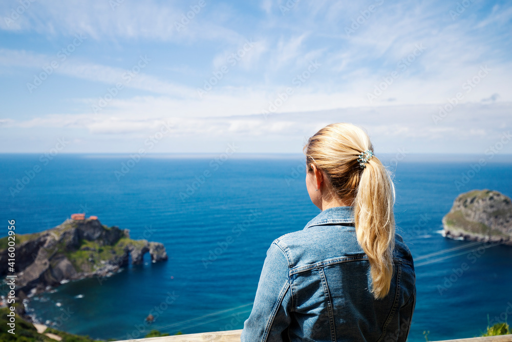 A lonely blonde in a denim jacket looks at the sea and rocks in the Bay of Biscay, Spain. Selective focus. Copy space
