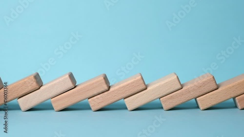 Domino effect, row of wooden domino falling down with yellow background.