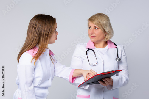 Amazed, shocked, dizzy medical doctors are discussing diagnosis during the conference pointing in sheet folder. Successful healthcare workers on gray background