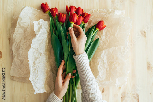 Billede på lærred Top view of hands wrapping red tulips in craft paper