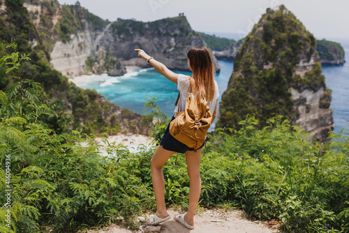 Back view of traveling  woman standing  on cliffs and tropical beach background. Freedom And adventure concept. Full length. Indonesia  Nusa Penida island.