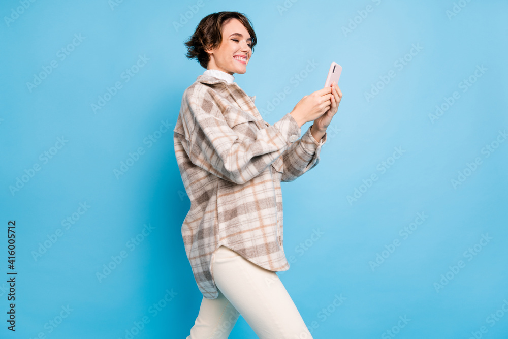 Profile side photo of young girl happy positive smile loo read browse smartphone isolated over blue color background Profile side photo of young girl happy positive smile loo read browse smartphone isolated over blue color background