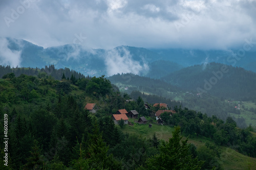 A view of the slopes of the hills covered with trees and villages, with misty mountains and stormy clouds in the background