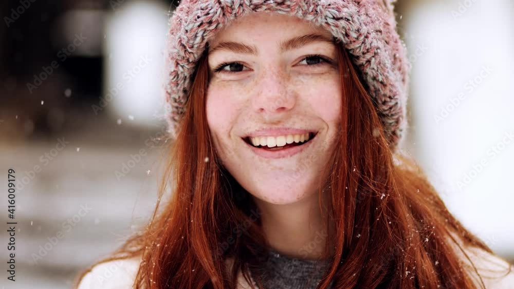 Close up portrait of cute charming face of young woman model with red hair, posing looking at camera, smiling and feeling happy. Winter beautiful street outdoor. Slow motion Close up portrait of cute charming face of young woman model with red hair, posing looking at camera, smiling and feeling happy. Winter beautiful street outdoor. Slow motion