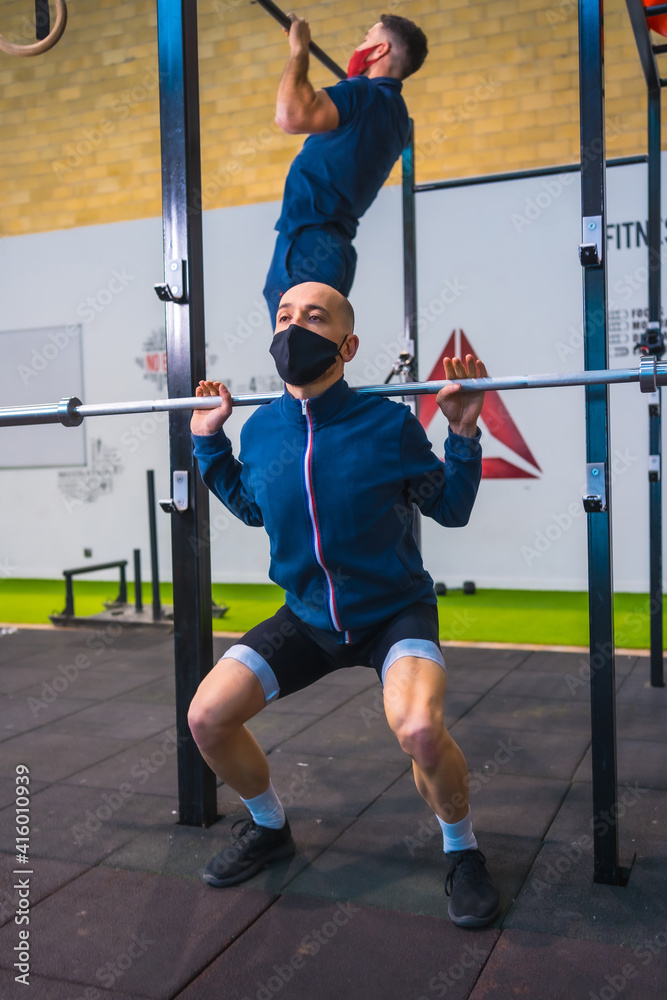 Obraz premium Two young people doing strength exercises in the gym in the coronavirus pandemic, a new normal. With protective face mask
