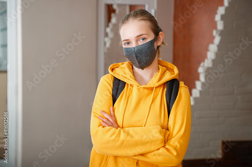 Young beautiful woman student wearing protective mask with backpack. Teen Girl blonde Caucasian teenager traveler with crossed arms in mask. Happy student in Reopen university campus covid 19 lockdown