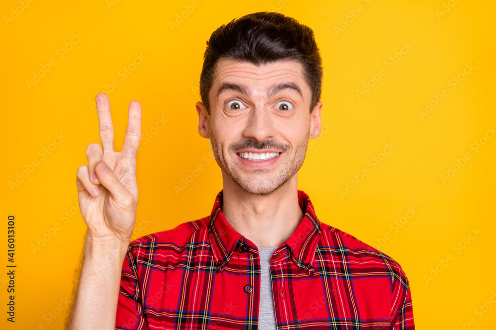 Photo of funny impressed young guy dressed red plaid shirt showing v-sign big eyes isolated yellow color background Photo of funny impressed young guy dressed red plaid shirt showing v-sign big eyes isolated yellow color background