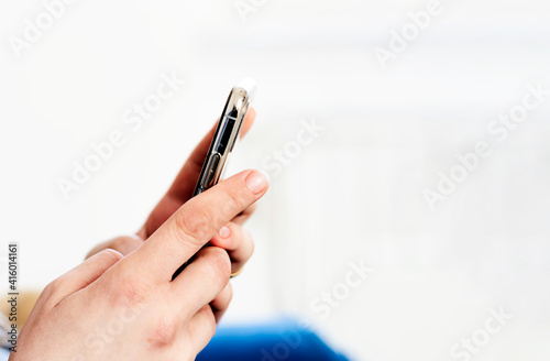 the hands of a young caucasian brunette woman while holding a smartphone typing on the touch screen.