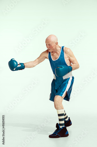 Fototapeta Naklejka Na Ścianę i Meble -  Kick. Senior man wearing sportwear boxing on studio background. Caucasian male model in great shape stays active and sportive. Concept of sport, activity, movement, wellbeing. Copyspace, ad.