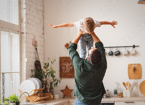 Anonymous father lifting cute son above head in kitchen