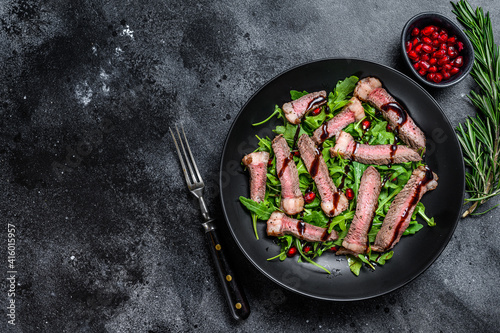 Grilled Beef Steak salad with arugula, pomegranate and greens vegetables. Black background. Top view. Copy space