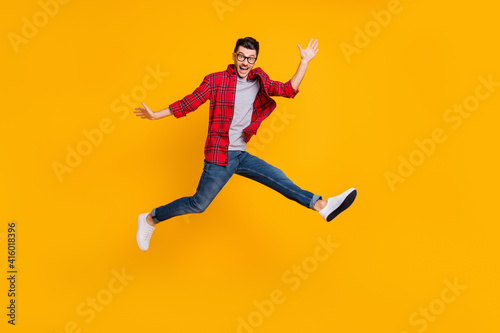 Full length photo of funny young man wear checkered shirt eyewear jumping high isolated yellow color background