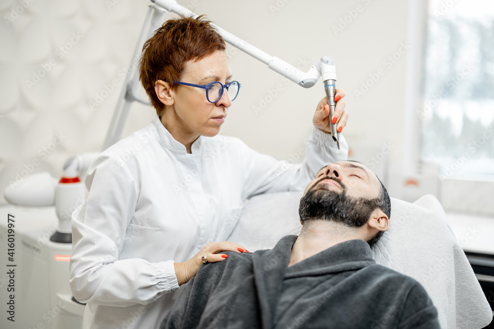 Obraz premium Cosmetologist doing laser facelifting procedure to man in beauty clinic. Anti-age, non-invasive, non-surgical laser facelift for natural-looking results concept. 