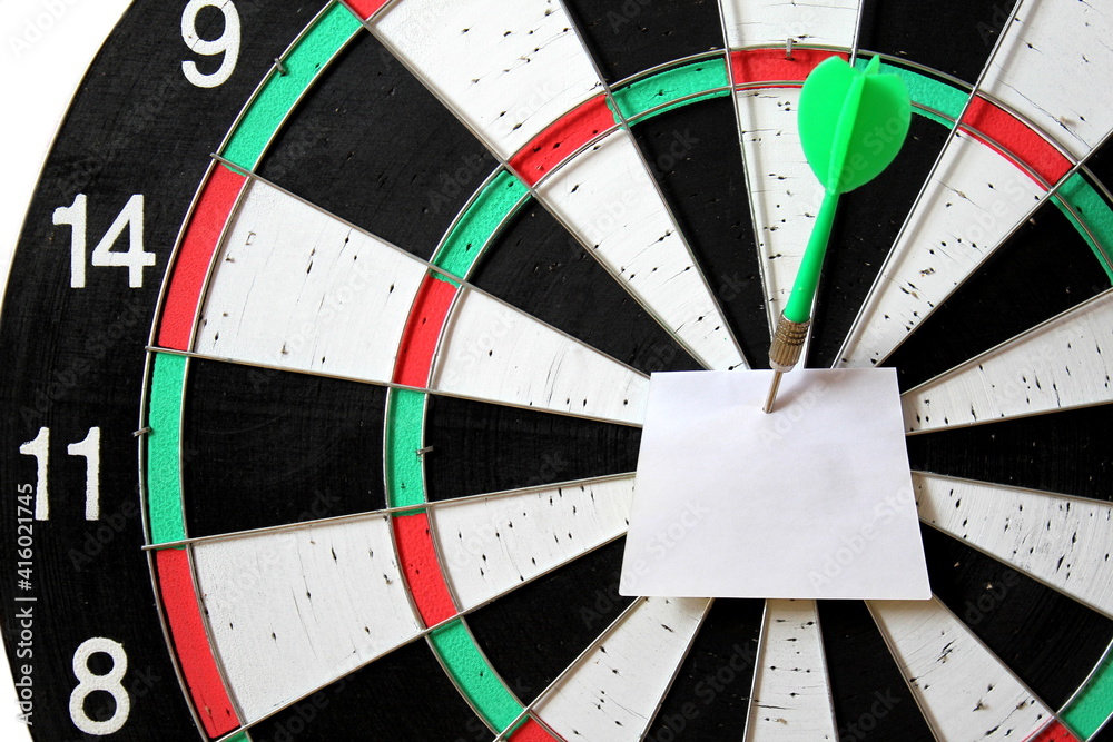 A piece of small paper stabbed with a dart in a dart board A piece of small paper stabbed with a dart in a dart board
