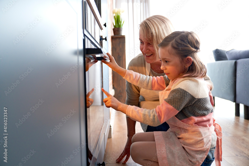 Side view of girl and grandma watching biscuits in kitchen oven Side view of girl and grandma watching biscuits in kitchen oven