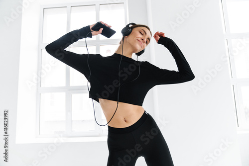 Fototapeta Naklejka Na Ścianę i Meble -  Happy woman dancing while listening music with headphones and smartphone