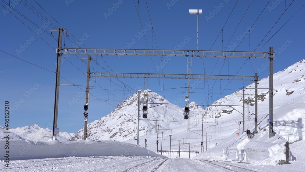 Switzerland Alps , Poschiavo - February 2021 Bernina Express, red train of Bernina pass in Ospizio Bernina station -  Unesco world heritage - Rhaetian railway with snow in a sunny day with blue sky