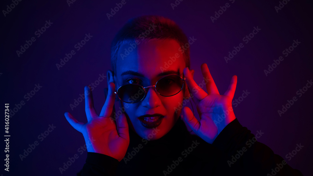 Portrait of a beautiful young woman with short hair in sunglasses in neon light