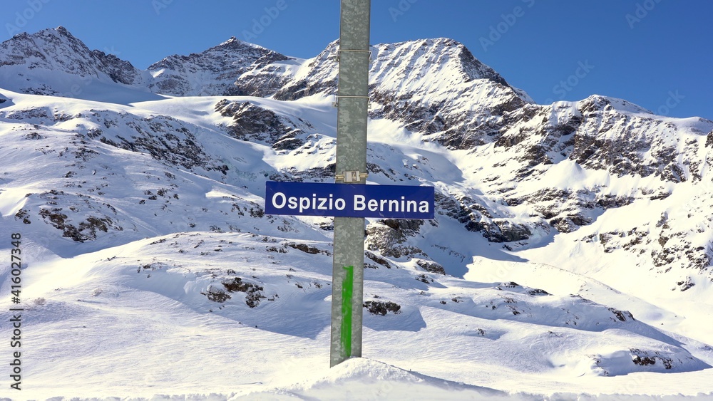 Switzerland Alps , Poschiavo - February 2021 Bernina Express, red train of Bernina pass in Ospizio Bernina station -  Unesco world heritage - Rhaetian railway with snow in a sunny day with blue sky
