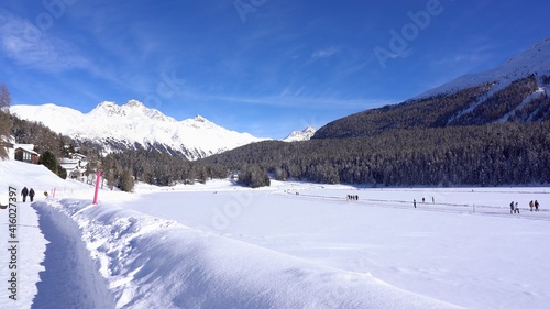 Europe, Switzerland , Saint Moritz February 2021 - Landscape with lake frozen in Sanit Moritz with people walking in the snow during Covid-19 Coronavirus epidemic lockdown - Bernina Express red train 