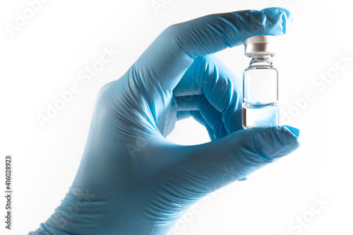Medical theme: doctor's hand in a blue glove holding a vial of transparent liquid for injection