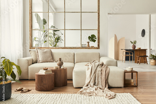 Modern interior of open space with design modular sofa, furniture, wooden coffee tables, plaid, pillows, tropical plants and elegant personal accessories in stylish home decor. Neutral living room.