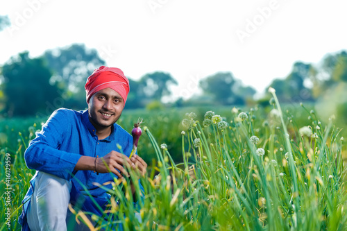 Young indian farmer holding onion crop in hand at agriculture field