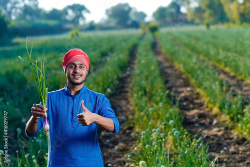 Young indian farmer holding onion crop in hand at agriculture field