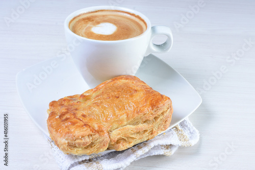 Cup of Colombian coffee, accompanied by baked bakery on white wooden background
