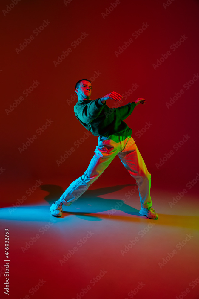 Freedom. Stylish sportive boy dancing hip-hop in stylish clothes on colorful background at dance hall in neon light. Youth culture, movement, style and fashion, action. Fashionable bright portrait.